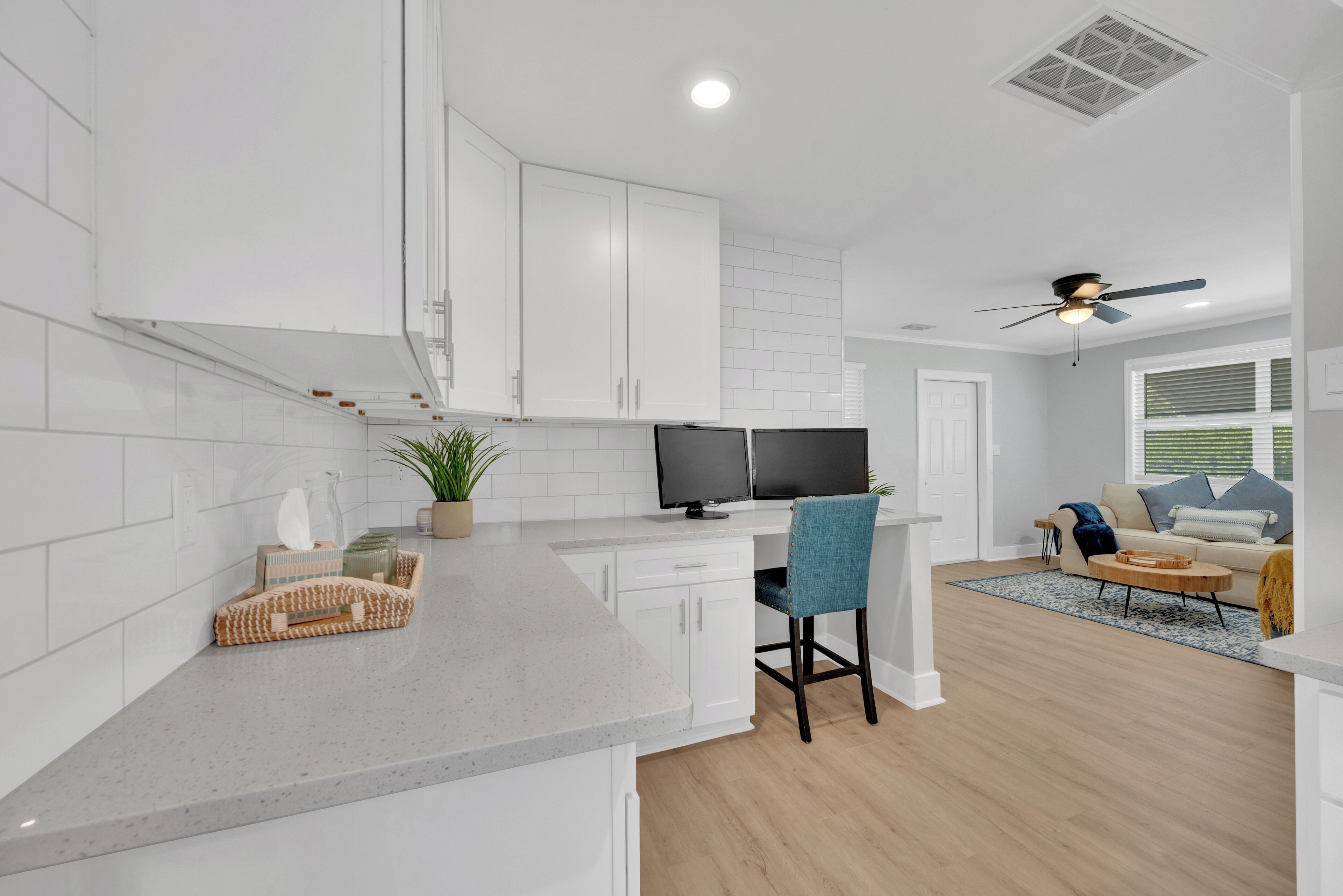 Une cuisine moderne avec des meubles blancs, un plan de travail en granit et un coin repas comprenant une chaise bleue et une table en bois.