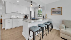 A modern kitchen with white cabinets, a stainless steel refrigerator, and a large island with bar stools. - Winter Getaway Stuart - Bring your truck, boat or RV - Large Fenced Yard (Stuart)