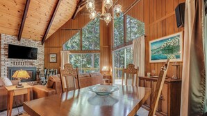 A wooden interior with a fireplace, dining table, and large windows. - Arnold Chalet Near Town & Calaveras Big Trees! (Arnold)