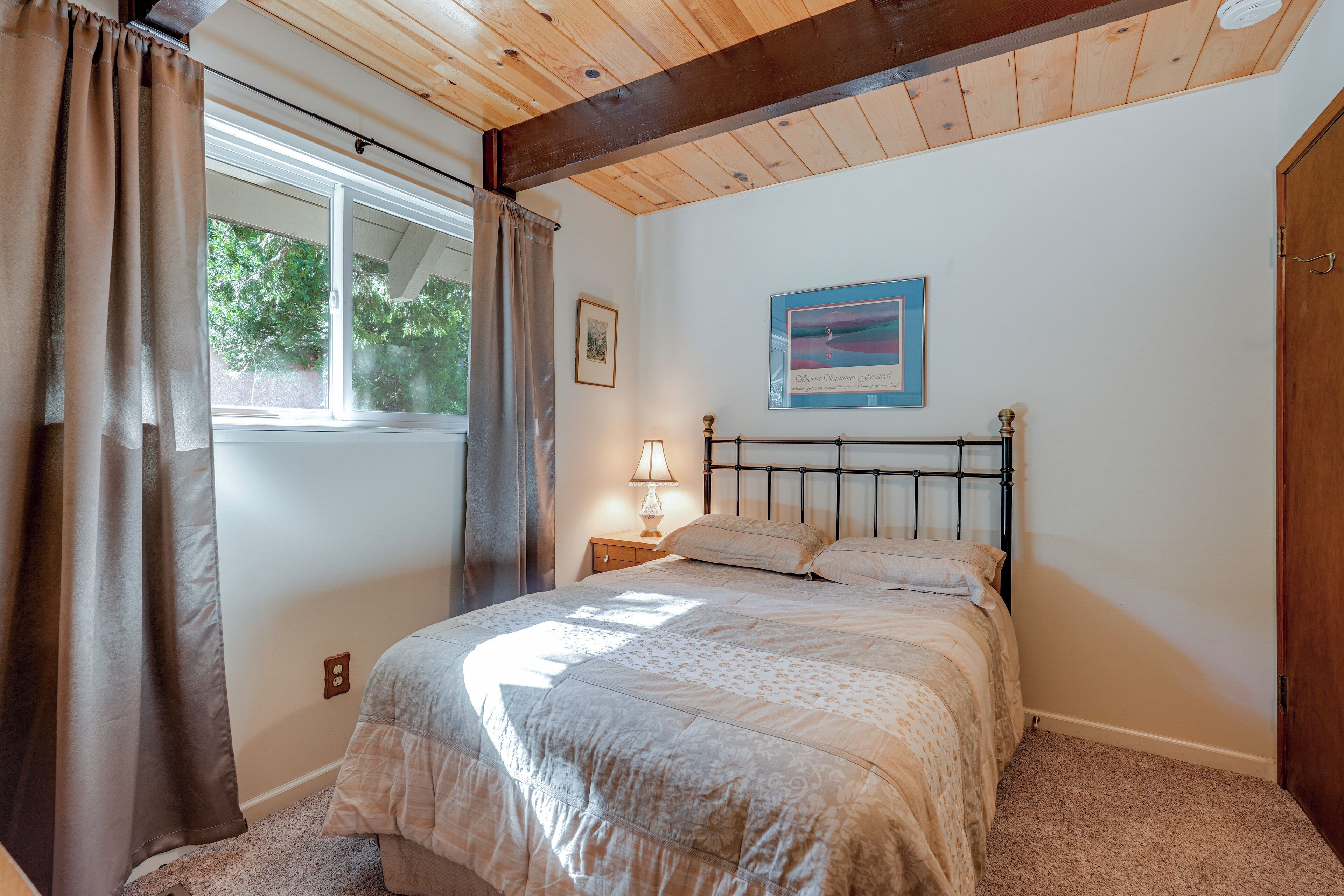 A bedroom with a bed, a nightstand, a lamp, a window with curtains, and a framed picture on the wall.
