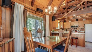 A wooden dining table with chairs, a chandelier, and a kitchen area with cabinets and a refrigerator. - Arnold Chalet Near Town & Calaveras Big Trees! (Arnold)