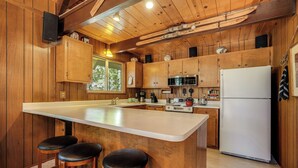 A kitchen with wooden cabinets, a large island with stools, a refrigerator, and a microwave. - Arnold Chalet Near Town & Calaveras Big Trees! (Arnold)