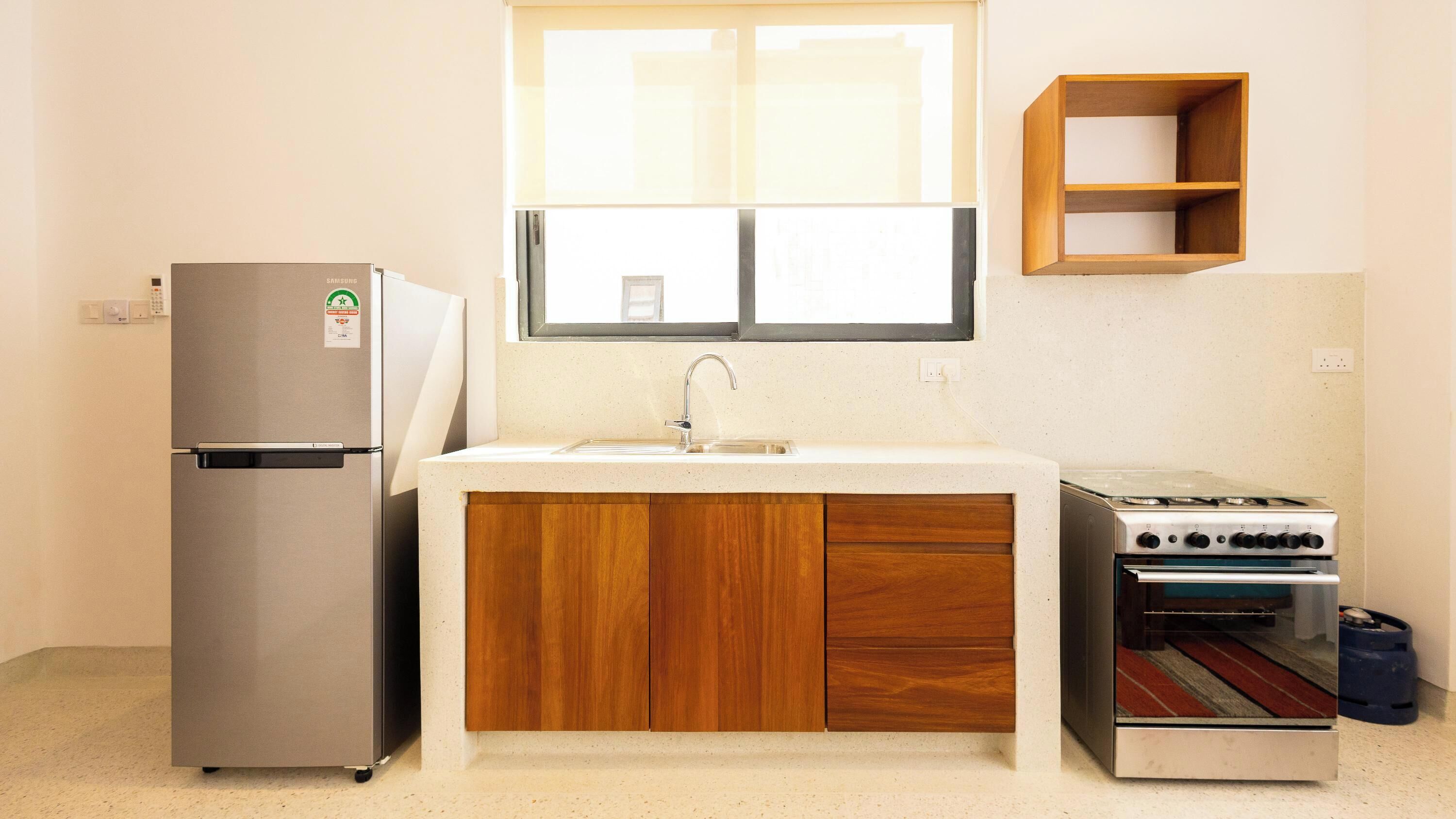 A compact kitchen with a refrigerator, sink, wooden cabinets, and a stove.
