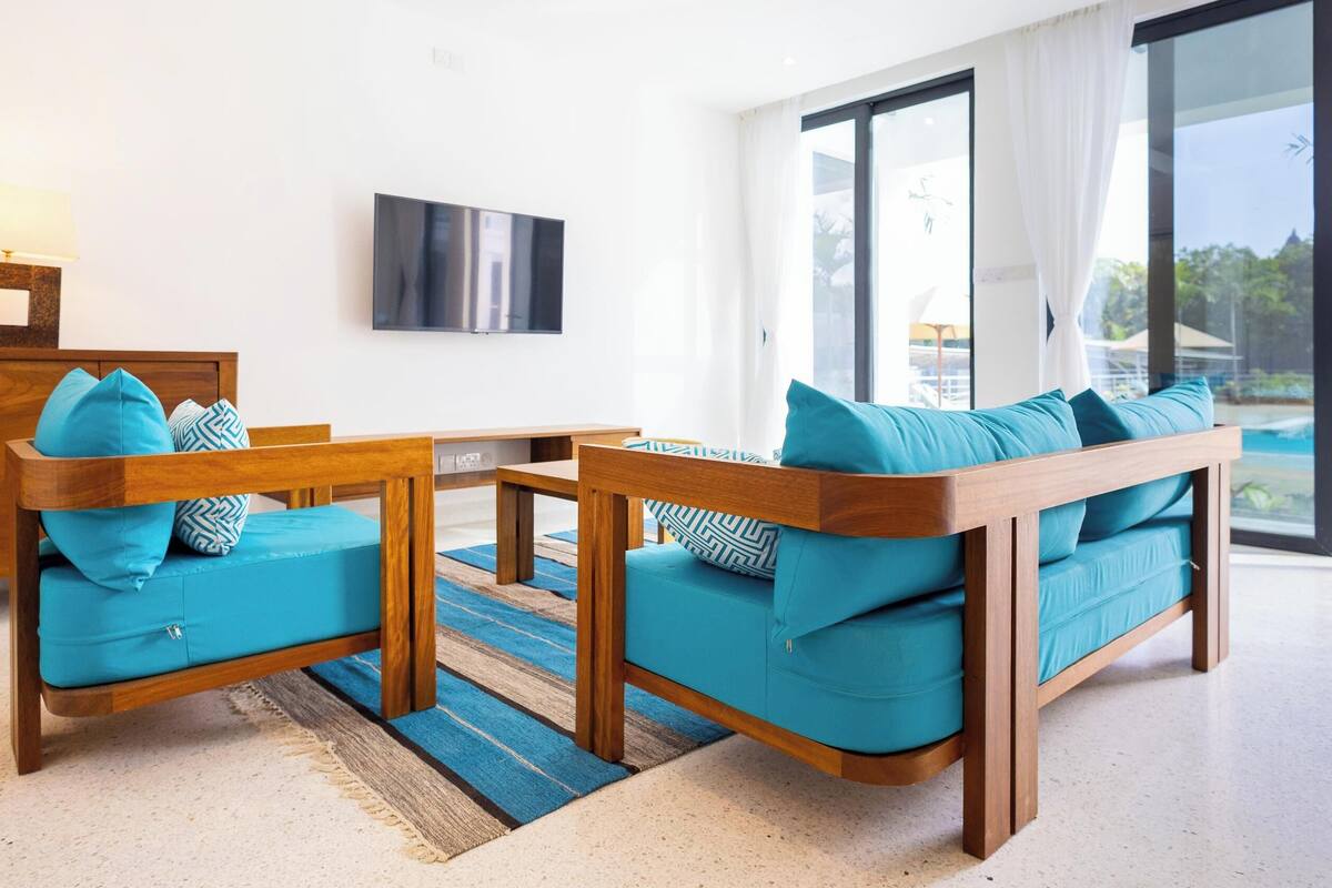 A modern living room with a sofa set, a wooden coffee table, and a flat-screen TV mounted on the wall.