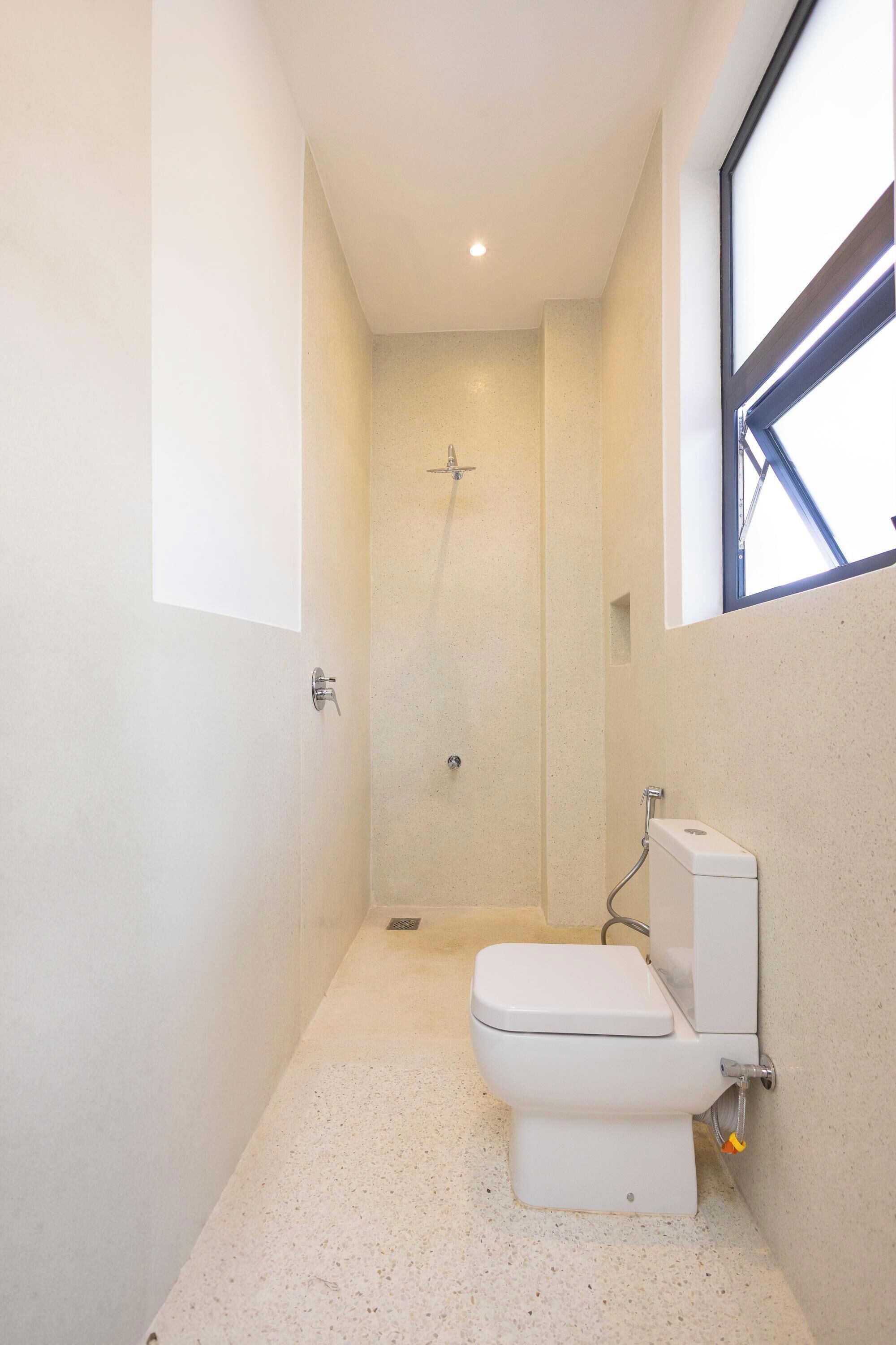 Et lille badeværelse med toilet, bruser og et vindue, der giver naturligt lys.
