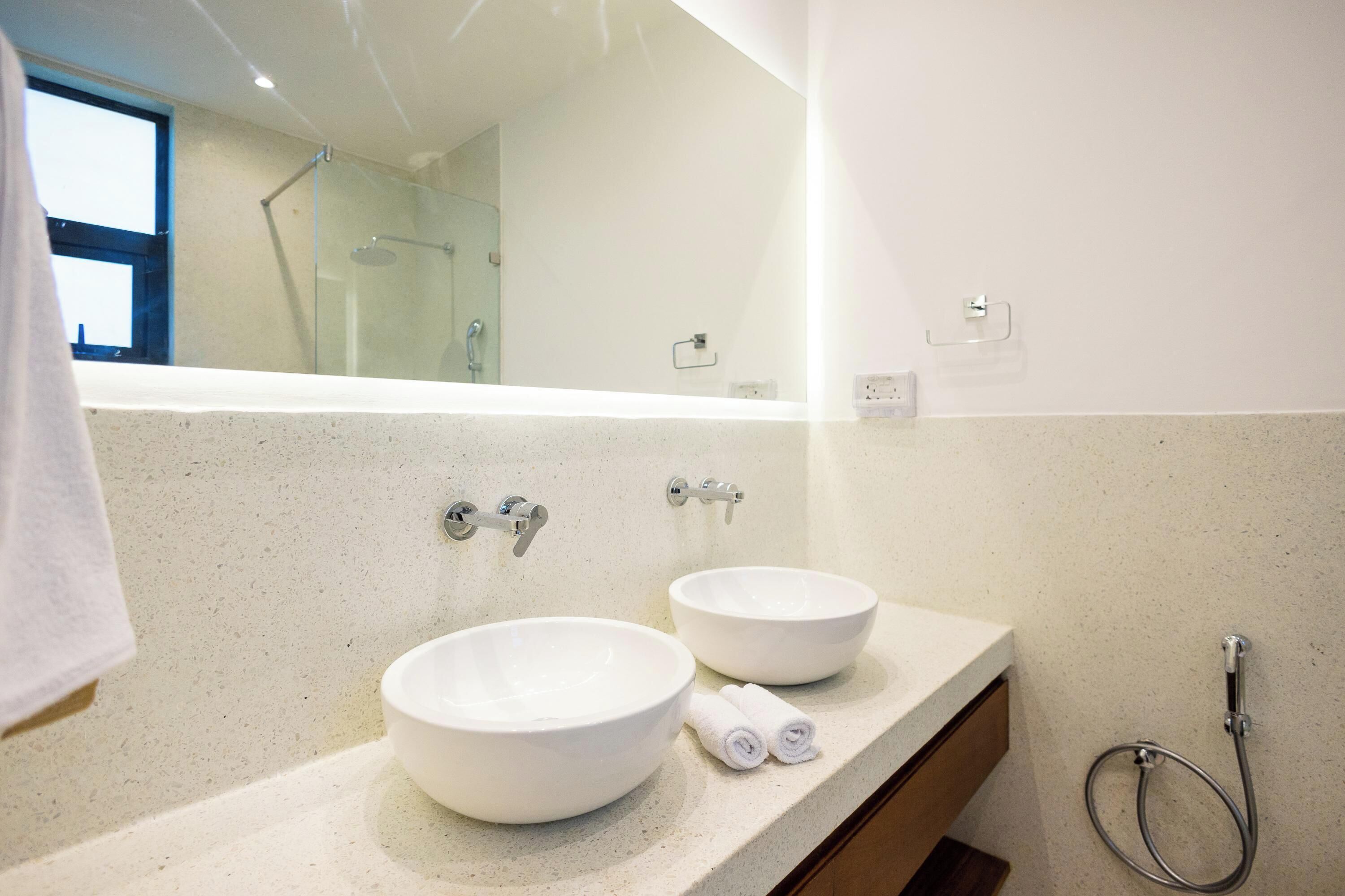 A bathroom with two white ceramic sinks, a glass shower enclosure, and a towel rack with towels.