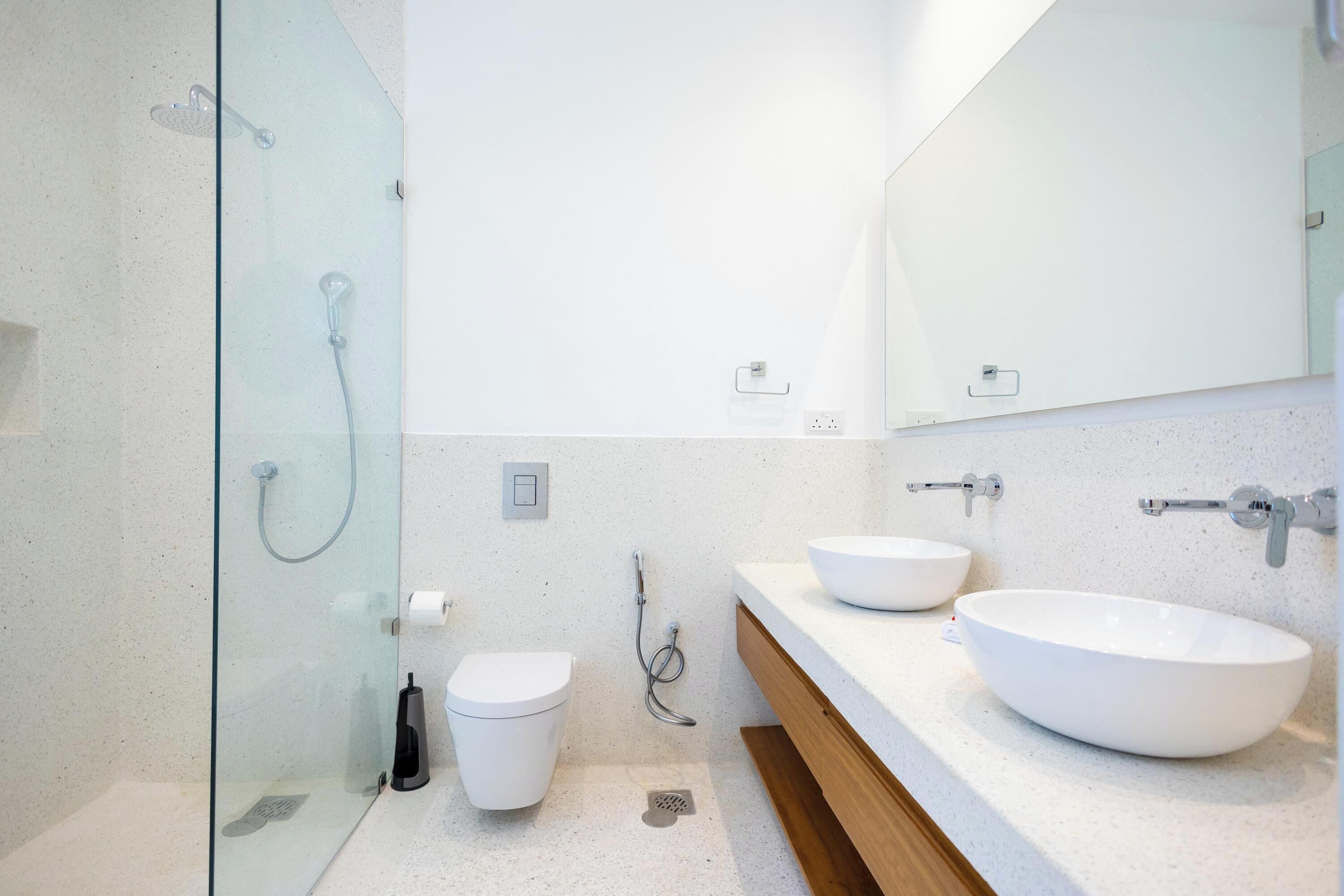 A modern bathroom with a glass shower enclosure, a toilet, and two sinks with a large mirror above.