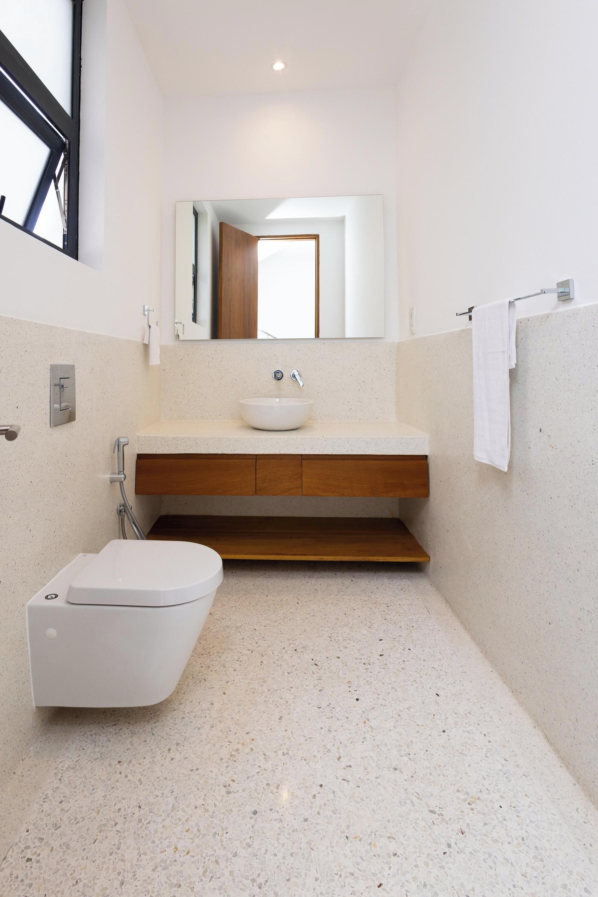 Un baño moderno con lavamanos blanco, tocador de madera y retrete.