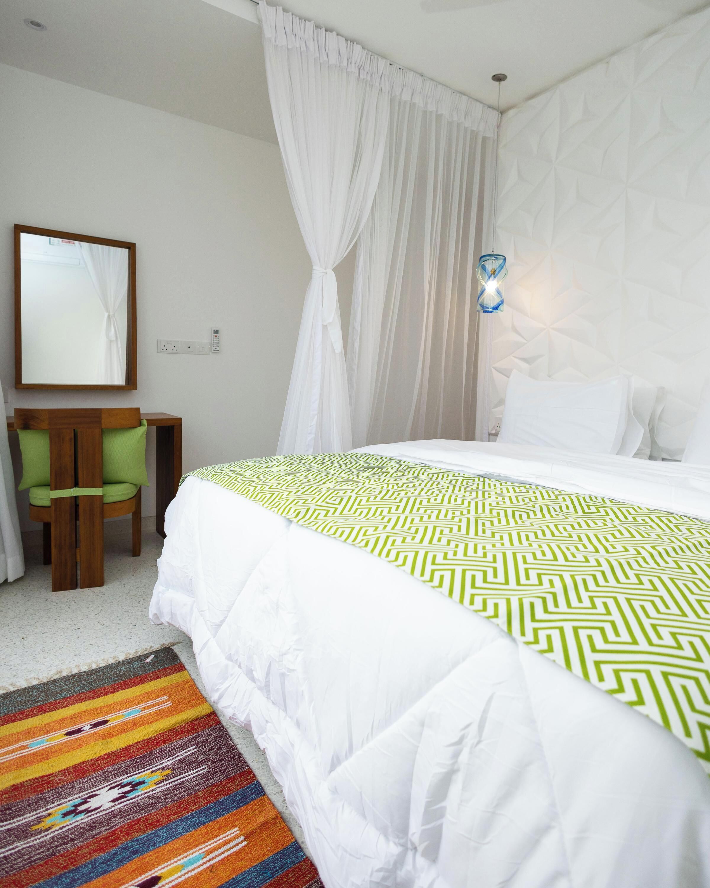 A hotel room with a bed, a chair, a mirror, and a patterned rug.