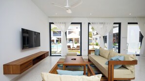Un salon moderne avec un canapé, une table basse, un téléviseur et une vue sur l’espace extérieur abritant la piscine.