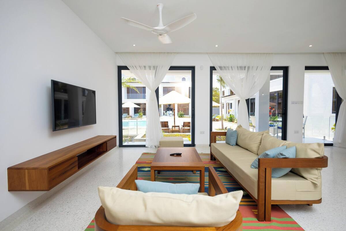 A modern living room with a sofa, coffee table, TV, and a view of the outdoor pool area.