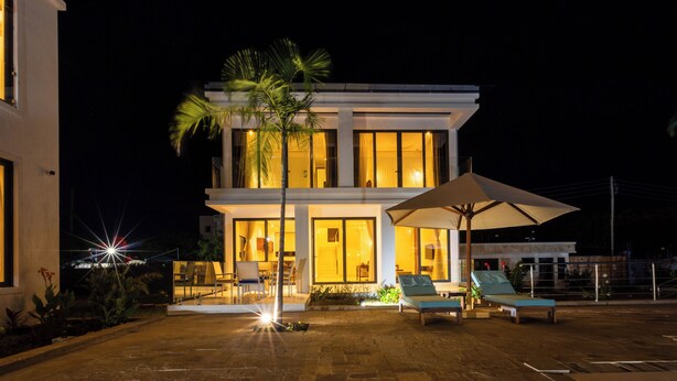 Une maison moderne à deux étages dotée d’un patio aménagé avec des chaises longues et un parasol.