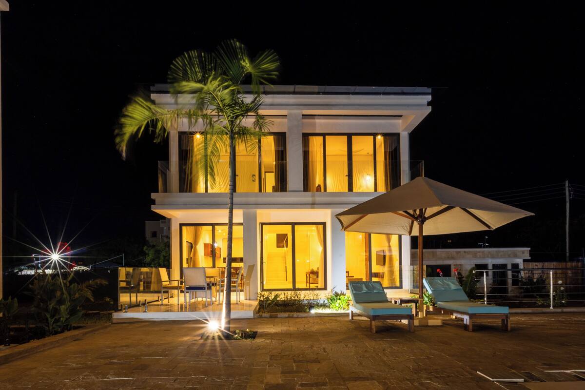 A modern two-story house with a patio area featuring lounge chairs and an umbrella.
