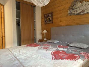 A bedroom with a wooden headboard, a bed with a patterned quilt, a bedside lamp, and a wooden wardrobe.