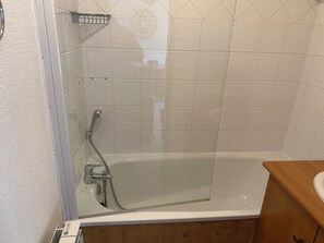 A bathroom with a glass-enclosed shower, a white bathtub, and a wooden vanity.