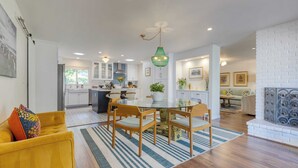 Een moderne keuken met witte kasten, een eethoek met een ronde tafel en stoelen, en een woonkamer met een bank en een open haard.