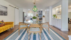 Een moderne keuken met witte kasten, een glazen eettafel en een groene kroonluchter.