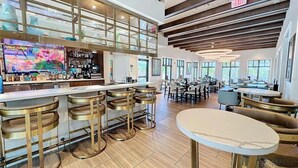 Un espace bar moderne doté d’un grand téléviseur, de tabourets de bar et d’un coin salon avec des tables et des chaises.