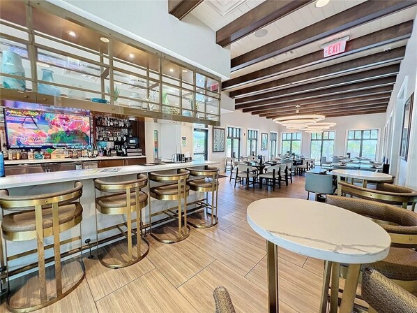 A modern bar area with a large TV, bar stools, and a seating area with tables and chairs.