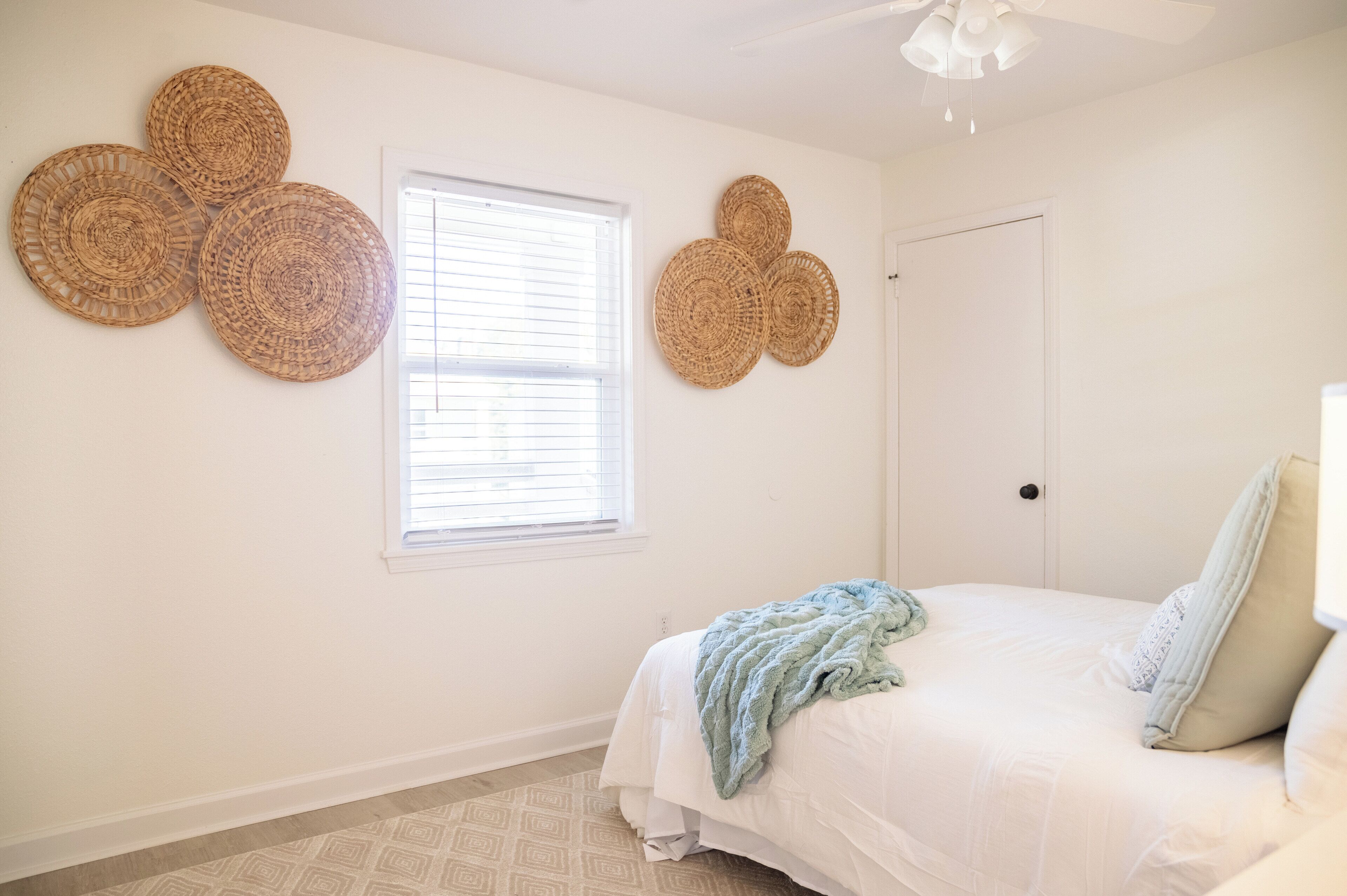 A bedroom with a bed, a window, and three woven wall decorations.