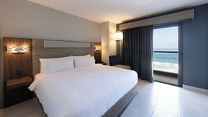 A modern hotel room with a large bed, a nightstand, a lamp, and a view of the ocean. - Holiday Inn Express & Suites Hotel Mazatlan by IHG (Mazatlán)