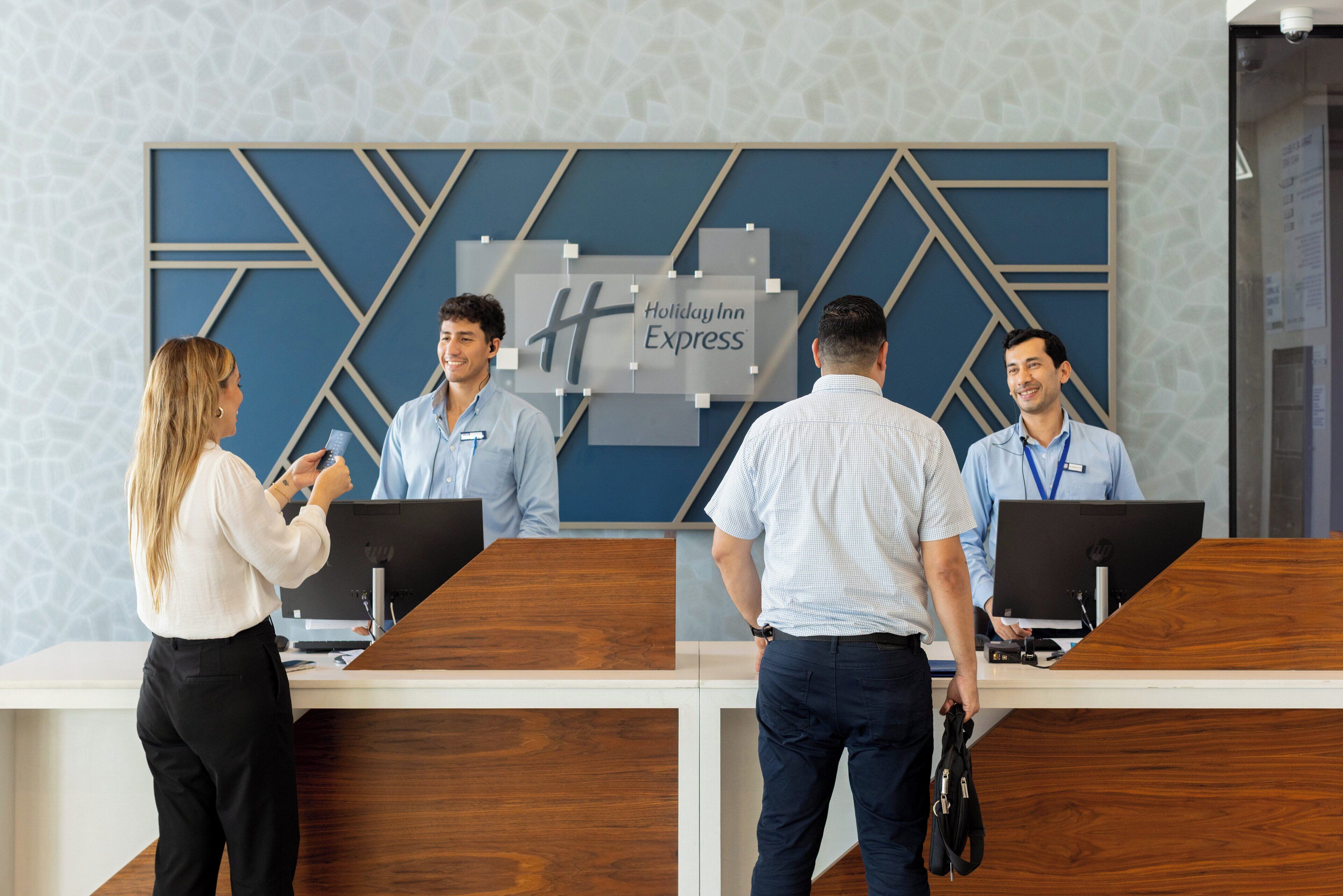 Una recepción con el letrero de Holiday Inn Express, dos empleados y un huésped interactuando.