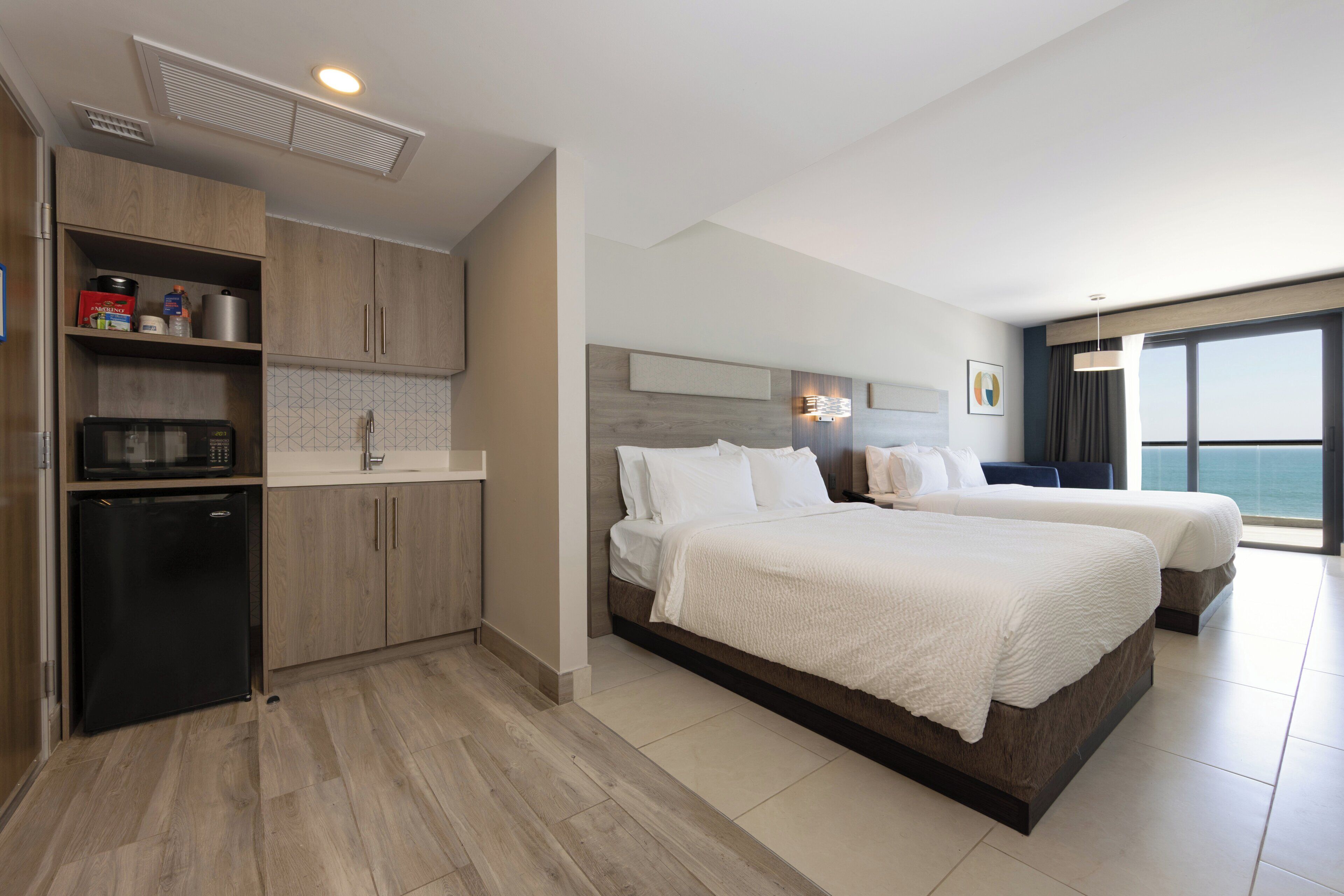 Een hotelkamer met een groot bed, een kitchenette en uitzicht op de oceaan.