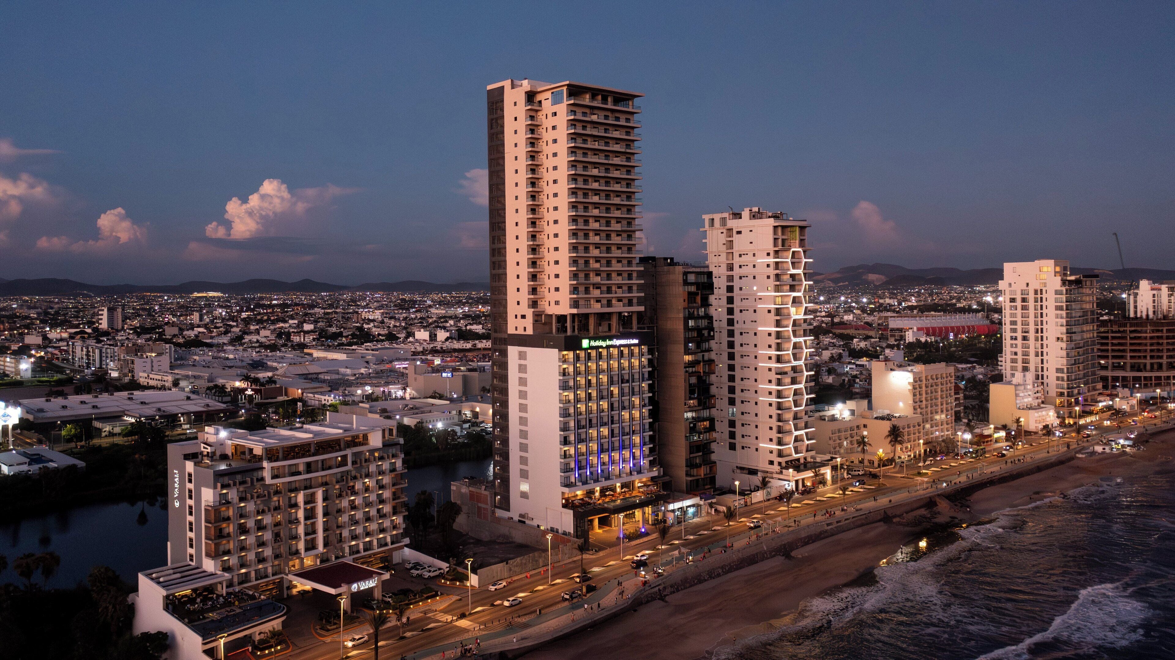 Un hotel de gran altura con varios pisos, un llamativo letrero Holiday Inn Express y ubicación frente a la playa.