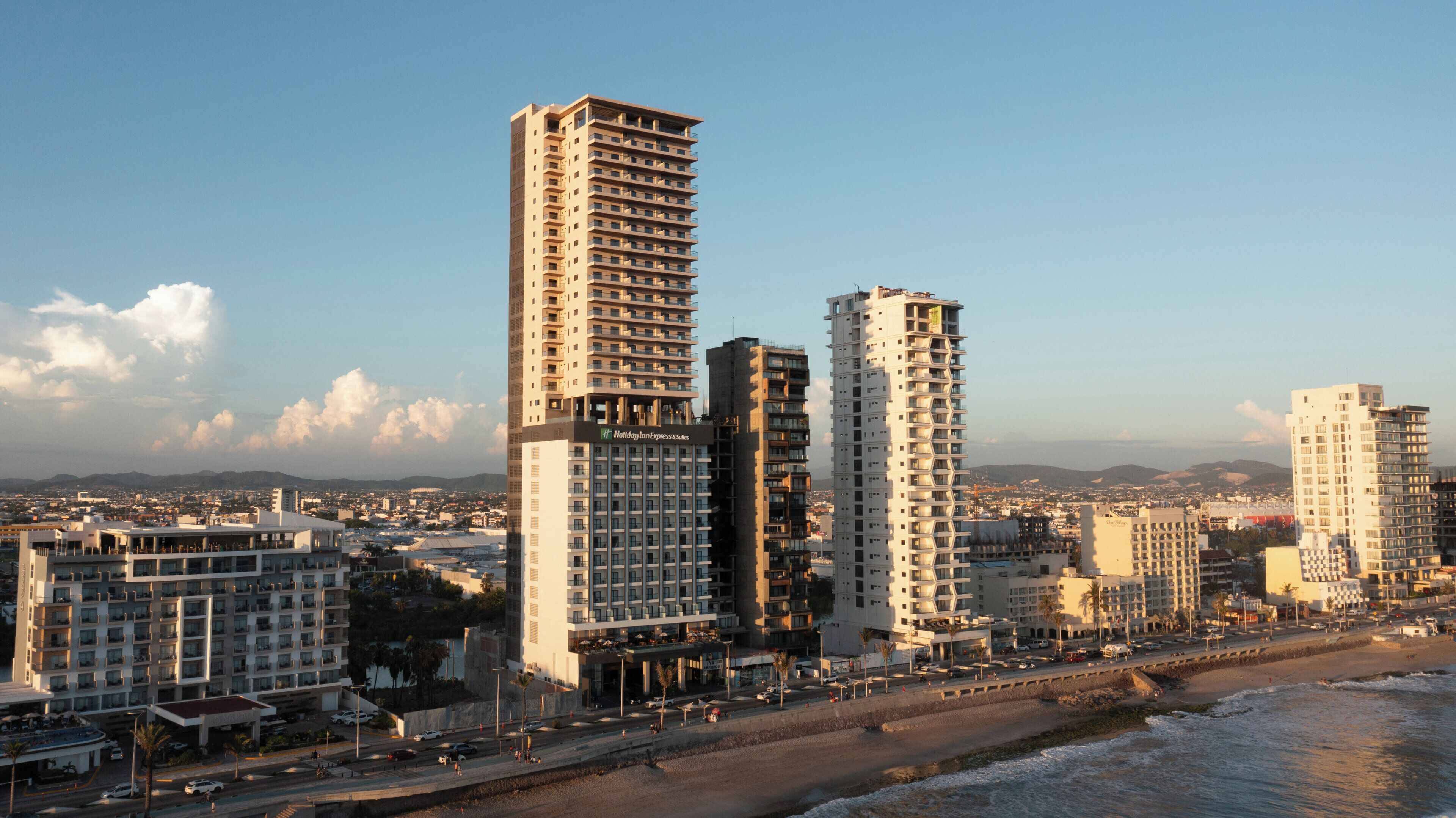 A coastal cityscape with high-rise buildings, including a hotel with balconies and a beachside location.