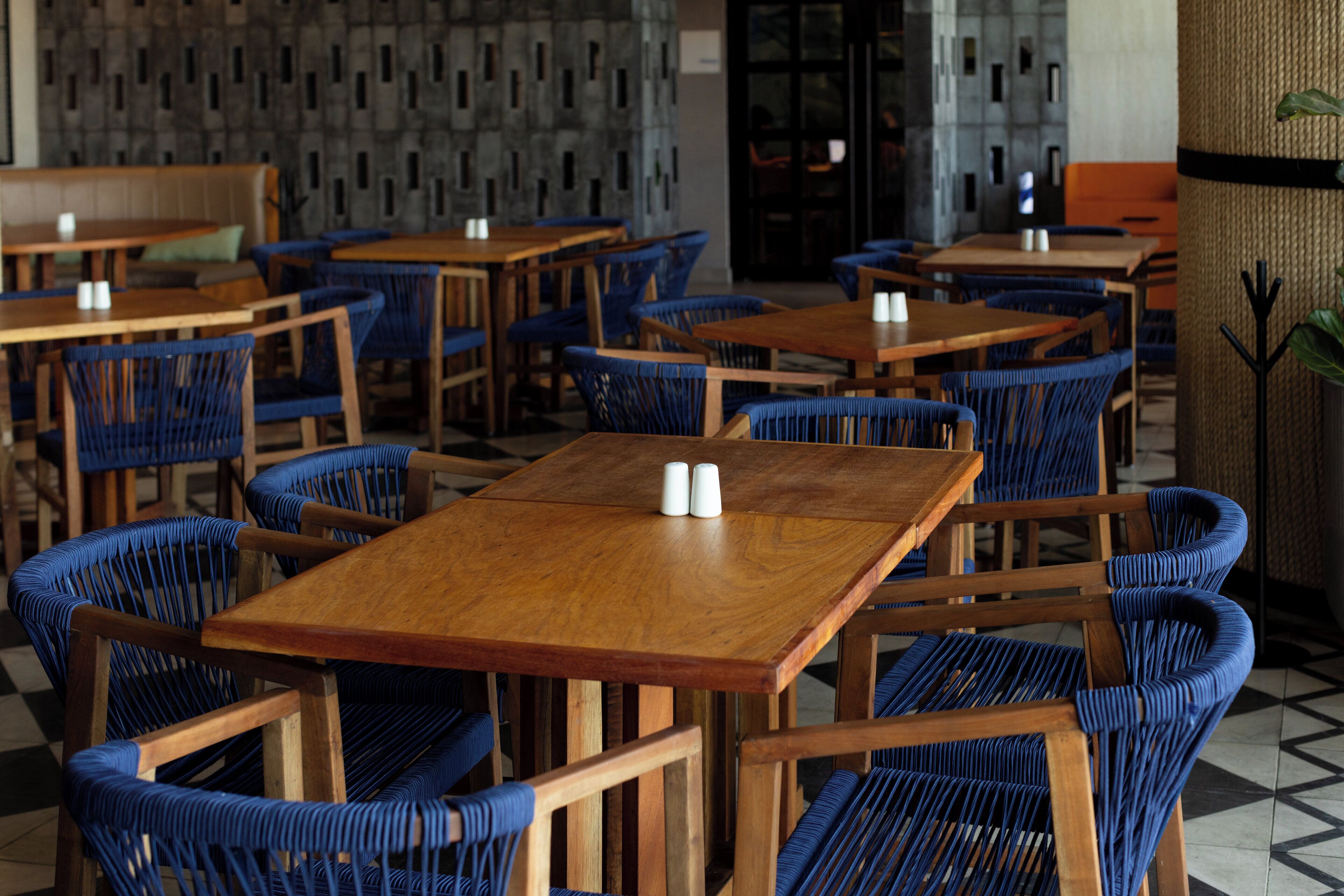 A restaurant with wooden tables and blue woven chairs.