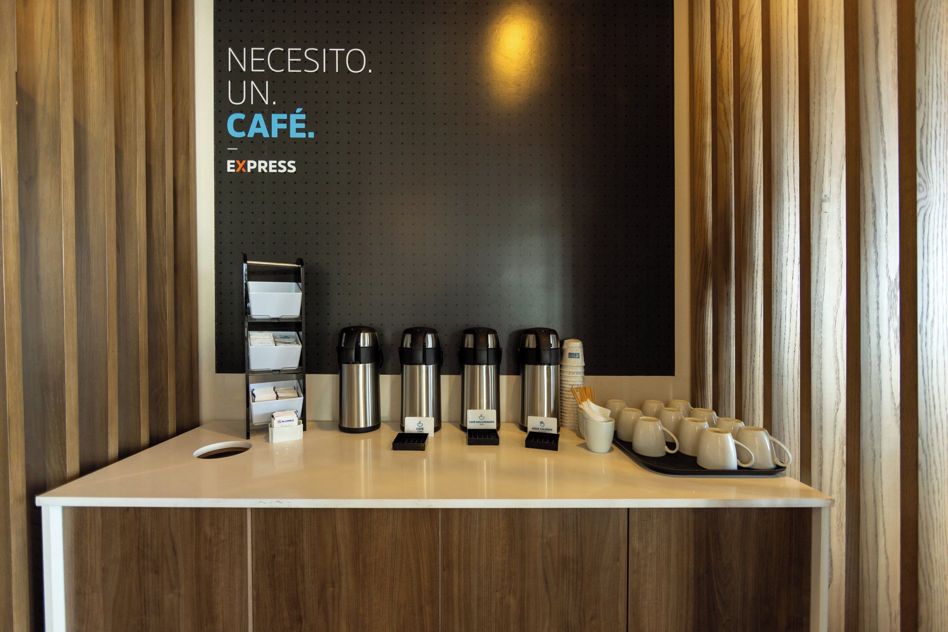 A coffee station with multiple coffee makers, cups, and a sign indicating the need for a coffee.