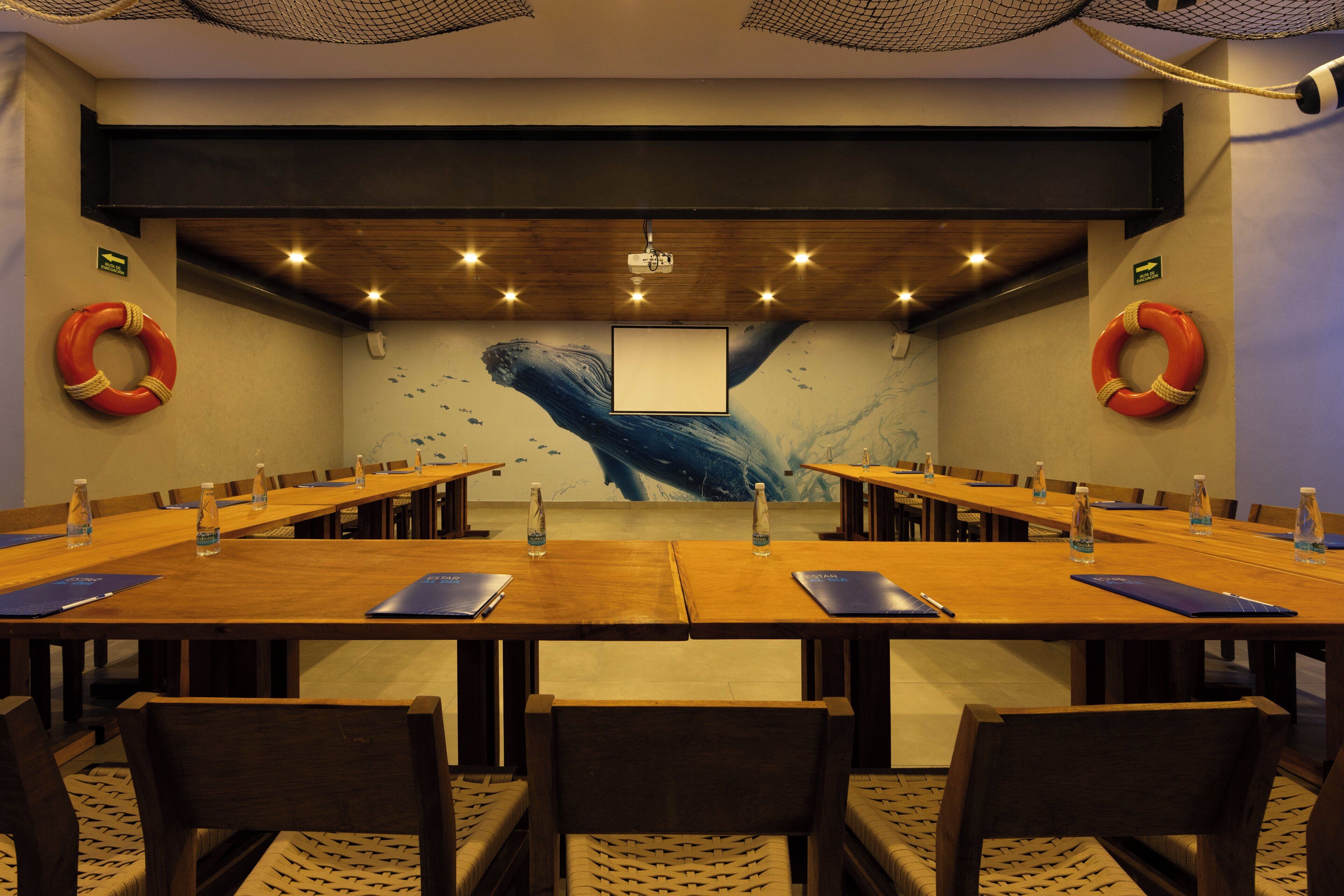 A conference room with a long wooden table, chairs, and a projector screen.