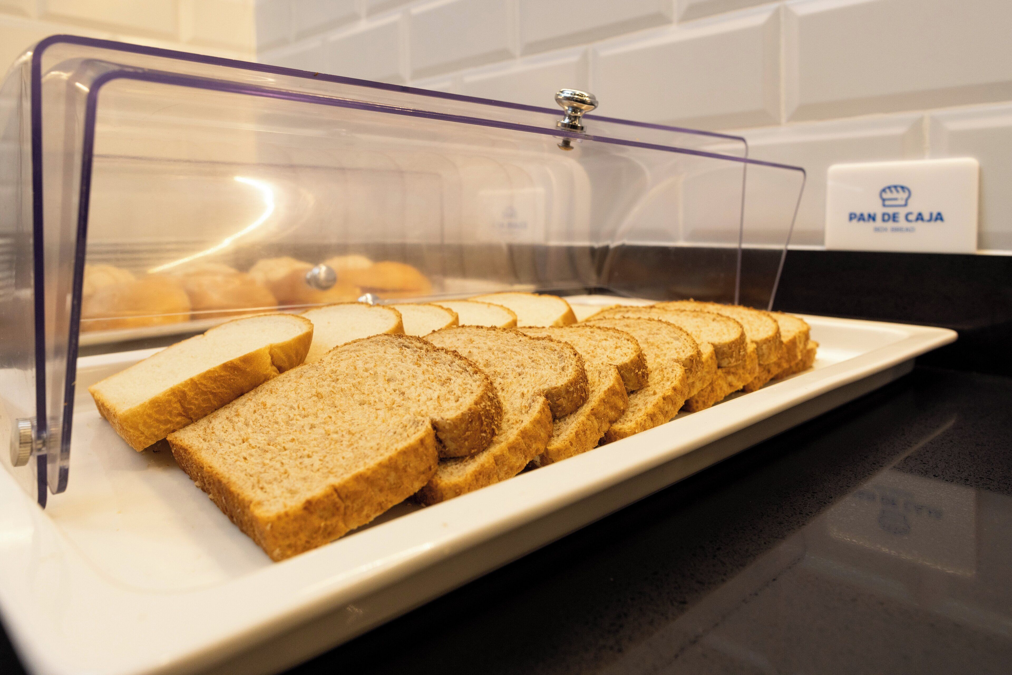 A clear display case with sliced bread and a sign reading "PAN DE CAJA".