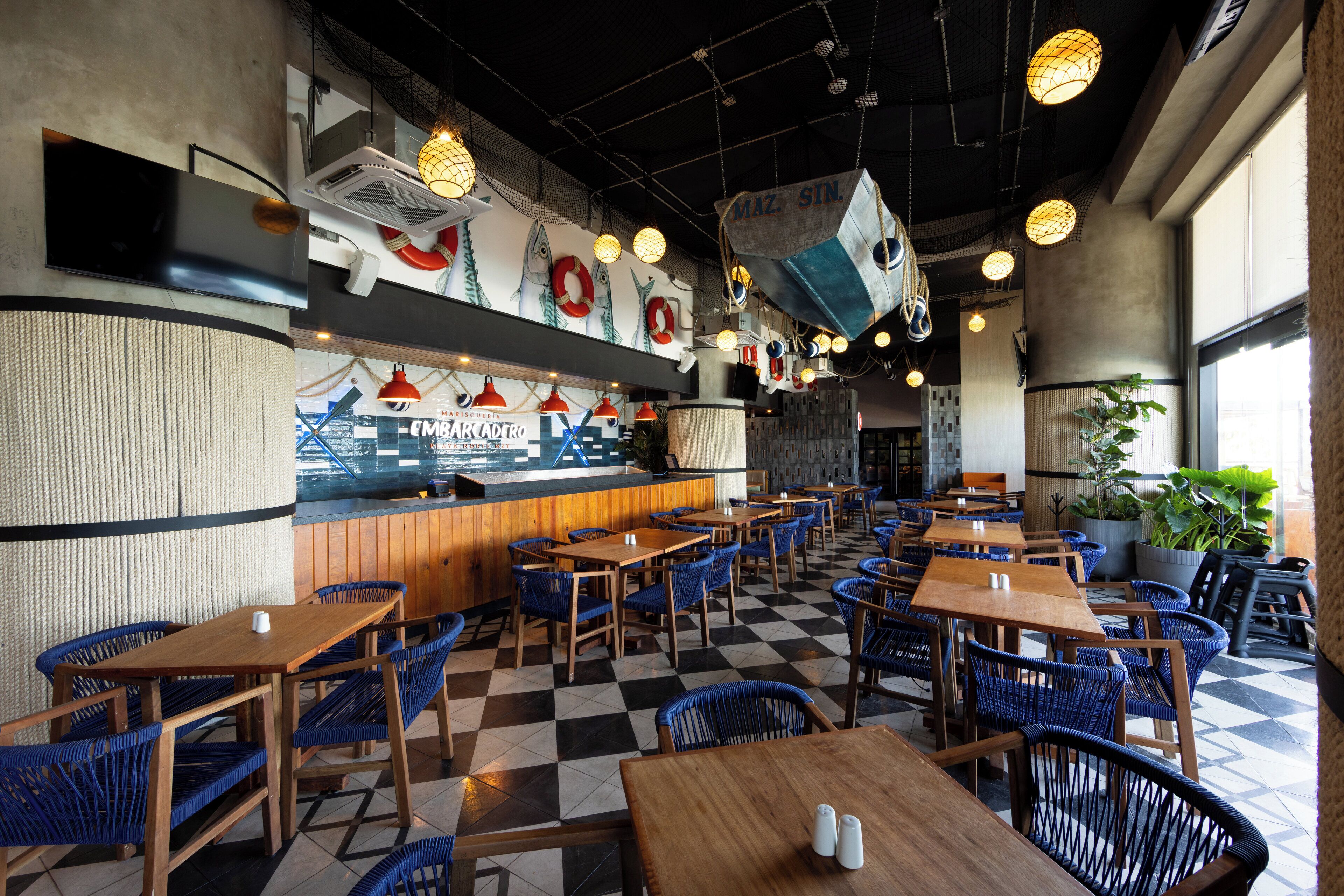 A restaurant with a checkered floor, wooden tables, blue chairs, and a counter with a fish mural.