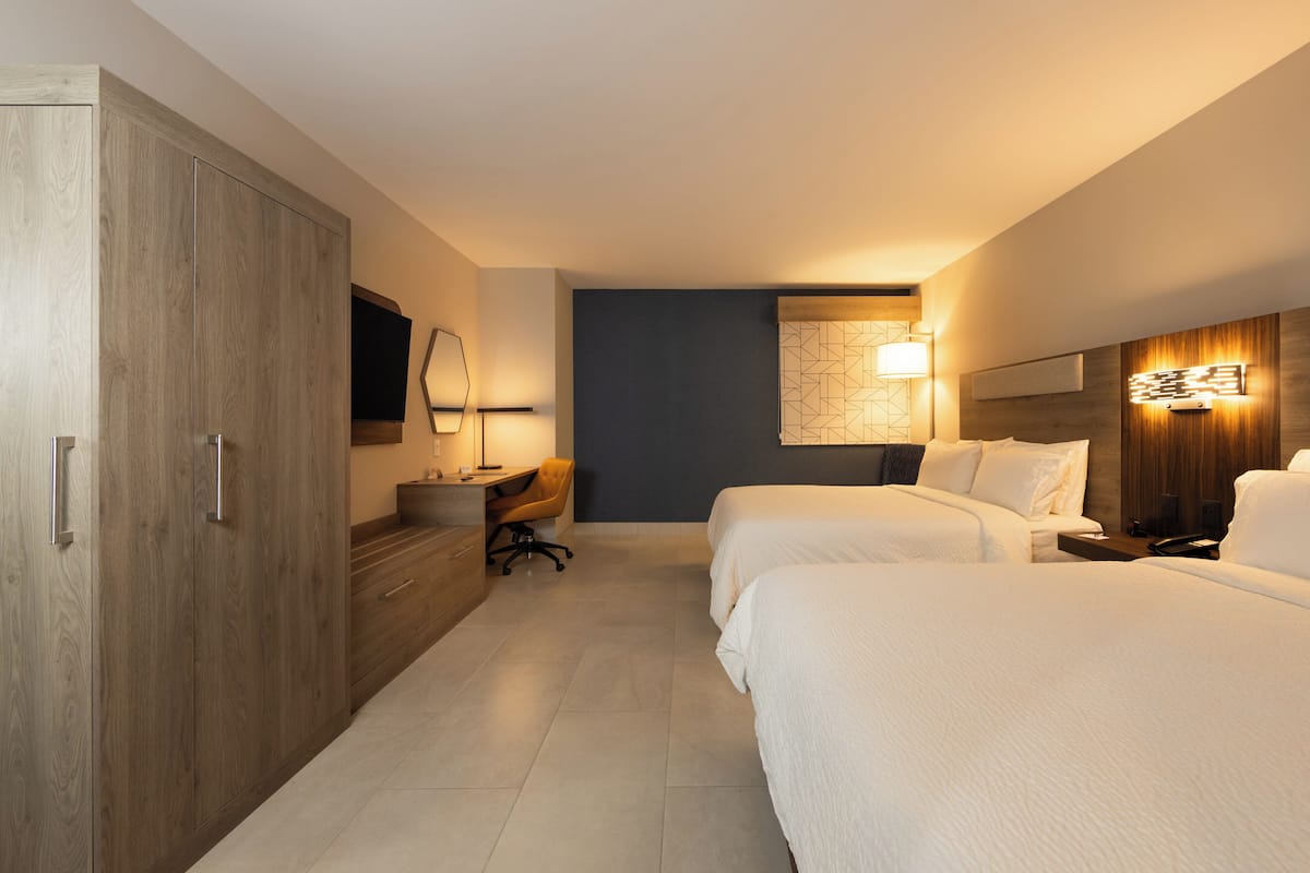 Ett hotellrum med två sängar, ett skrivbord med en stol, en garderob och en TV som är monterad på väggen.