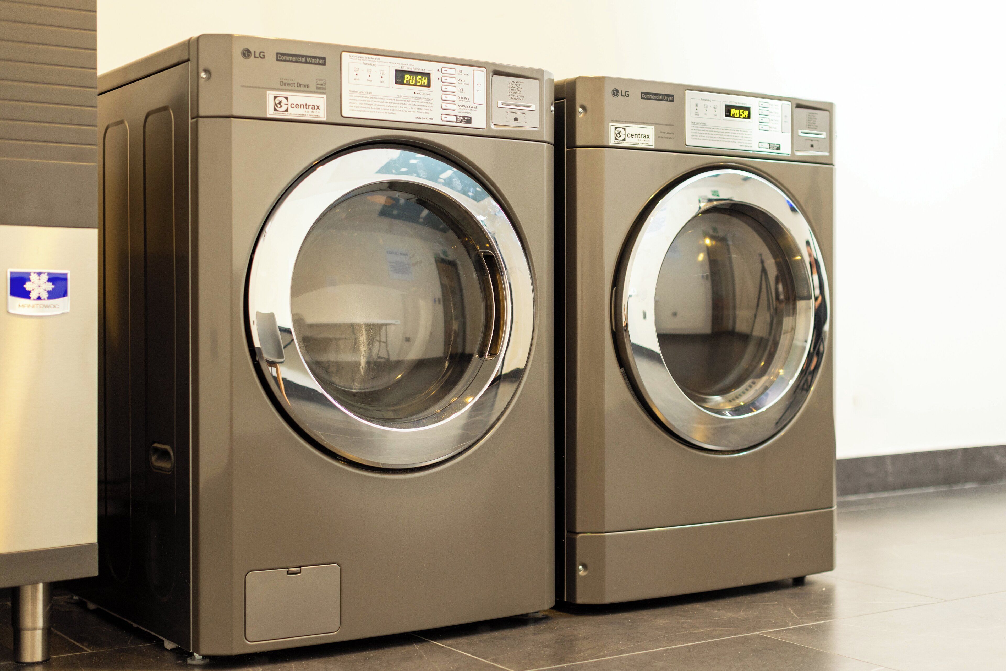 Two commercial washers with control panels, placed next to a wall.