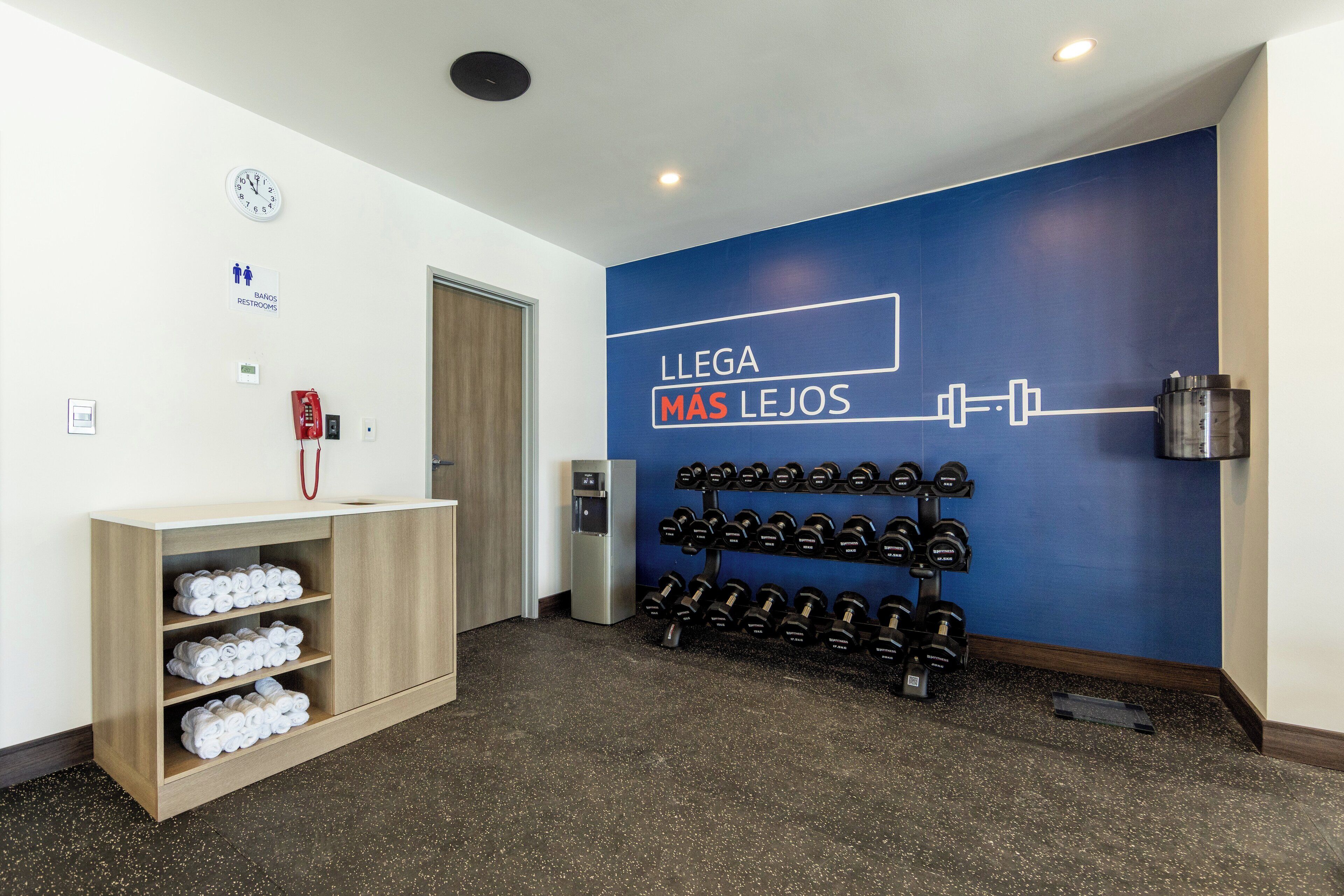 A gym area with a wall-mounted dumbbell rack, a water dispenser, and a wooden cabinet with towels.