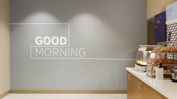 Una barra de desayuno con un letrero que dice 'GOOD MORNING', una máquina de café y pasteles.