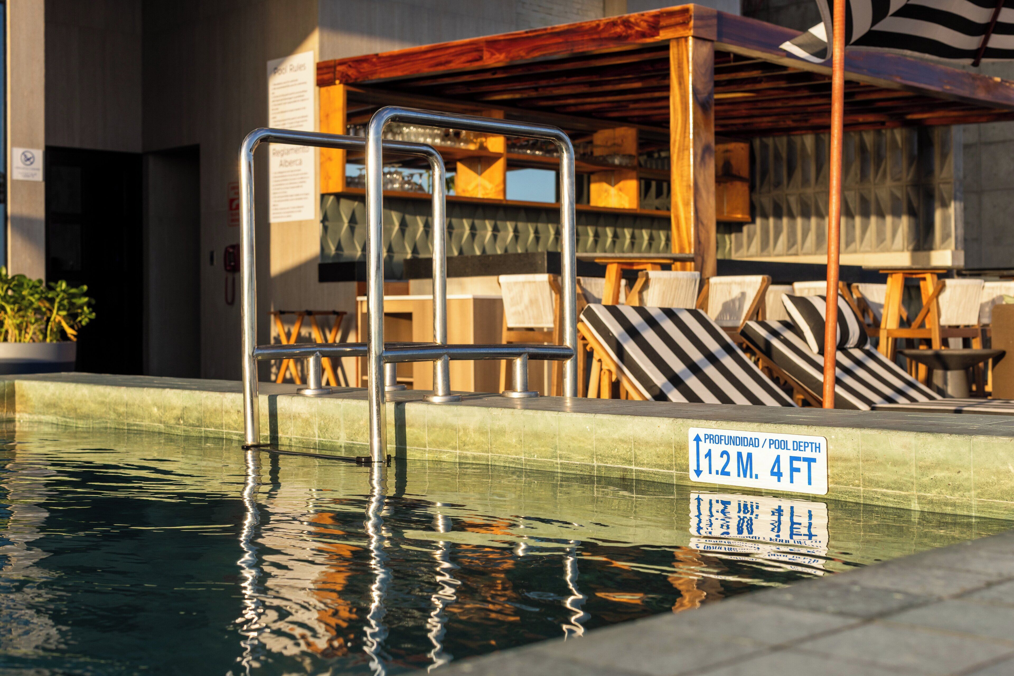 A pool with a depth sign, lounge chairs, and a wooden pergola.