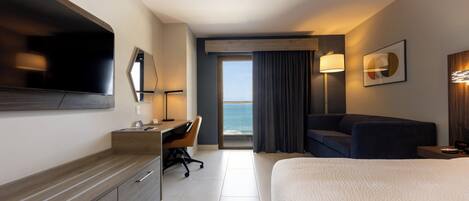 Habitación de hotel con cama, escritorio, silla y televisor grande.