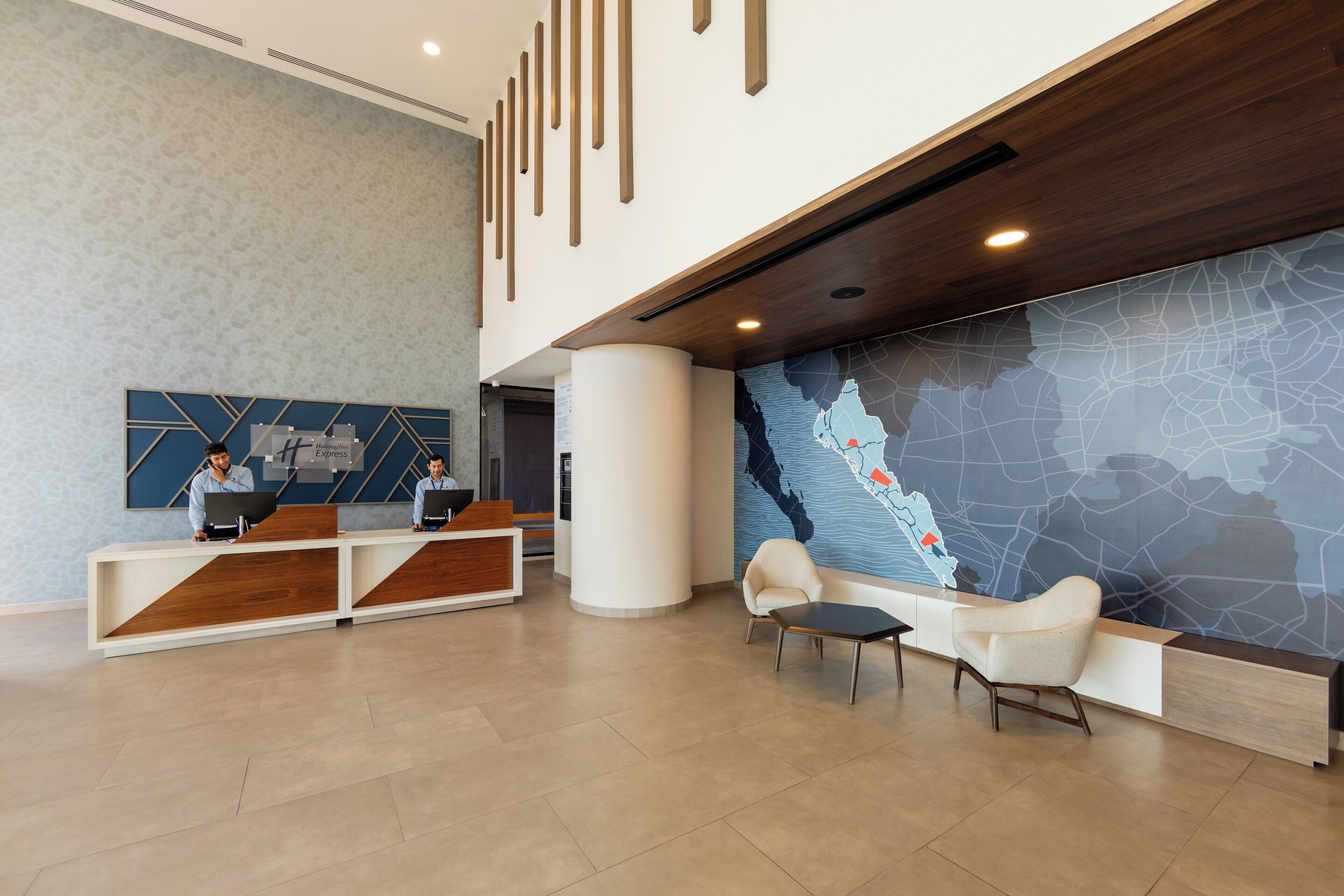 A modern reception area with a wooden reception desk, two staff members, a large map mural, and a seating area with two chairs.