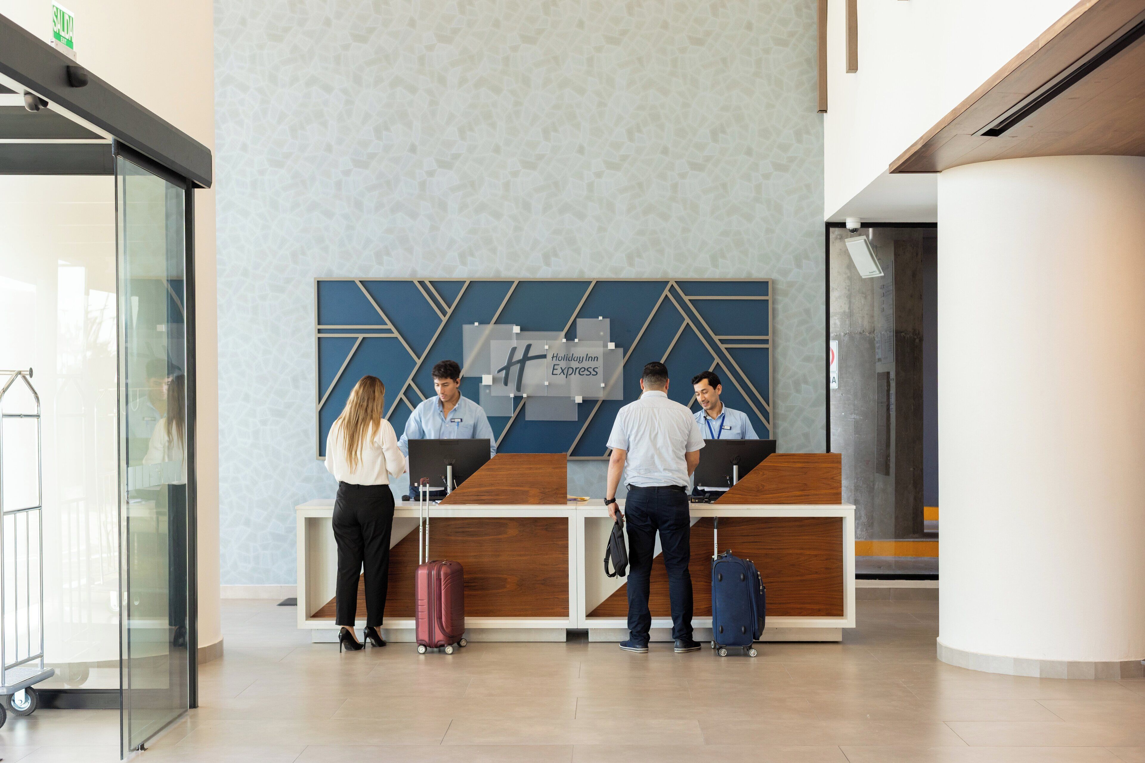 A reception desk with a modern design, a glass wall on the left, and a patterned wall behind the desk.