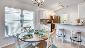 A modern kitchen with white cabinets, a central island, and a dining area with a round table and chairs.