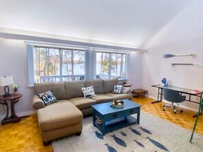A living room with a sofa, ottoman, coffee table, and a view of a lake through large windows.