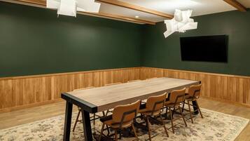 A conference room with a long table, six chairs, a wooden floor, a green wall, and a mounted TV.