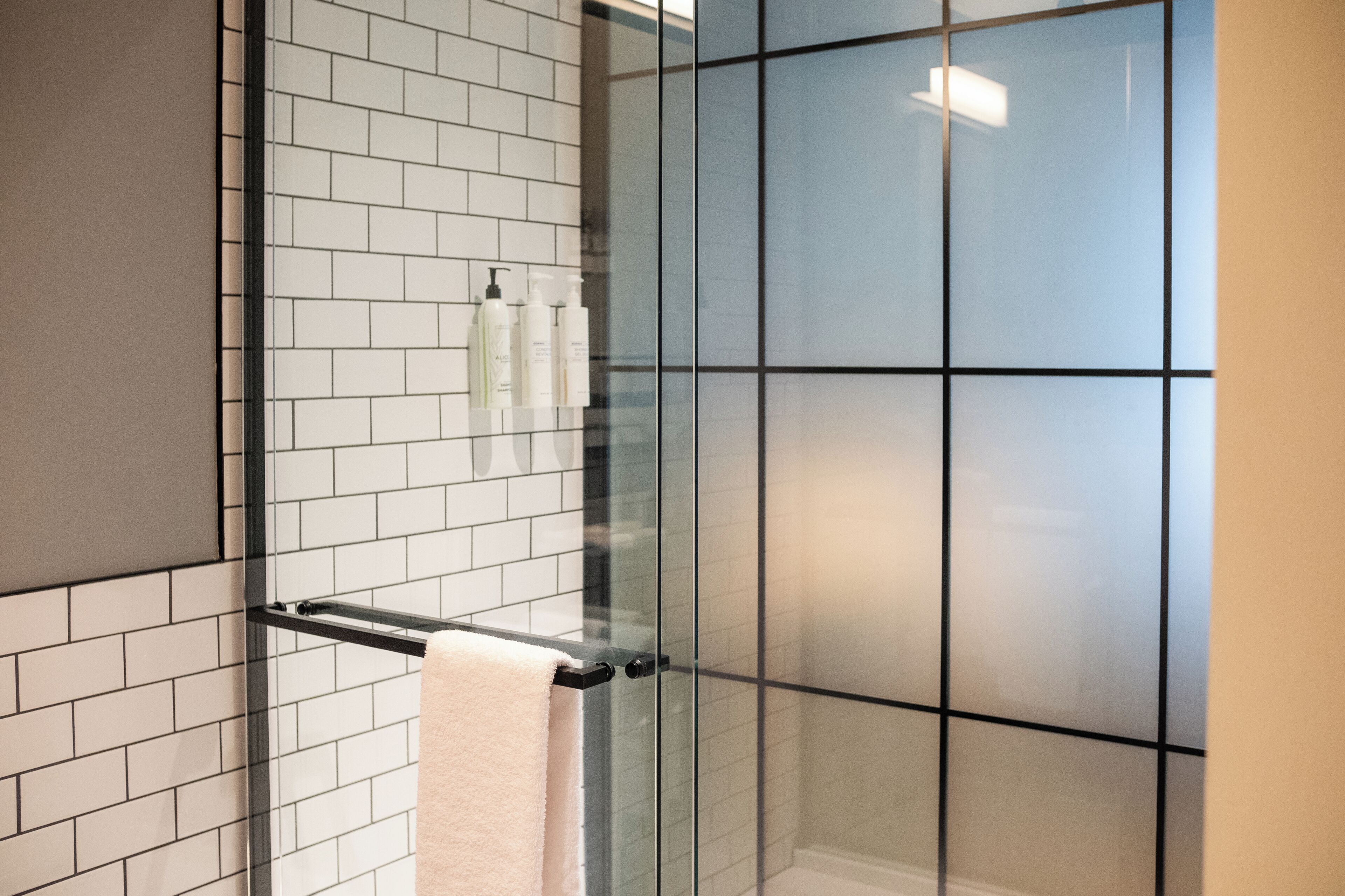 A modern bathroom with white subway tiles, a glass shower enclosure, and a towel rack with toiletries.