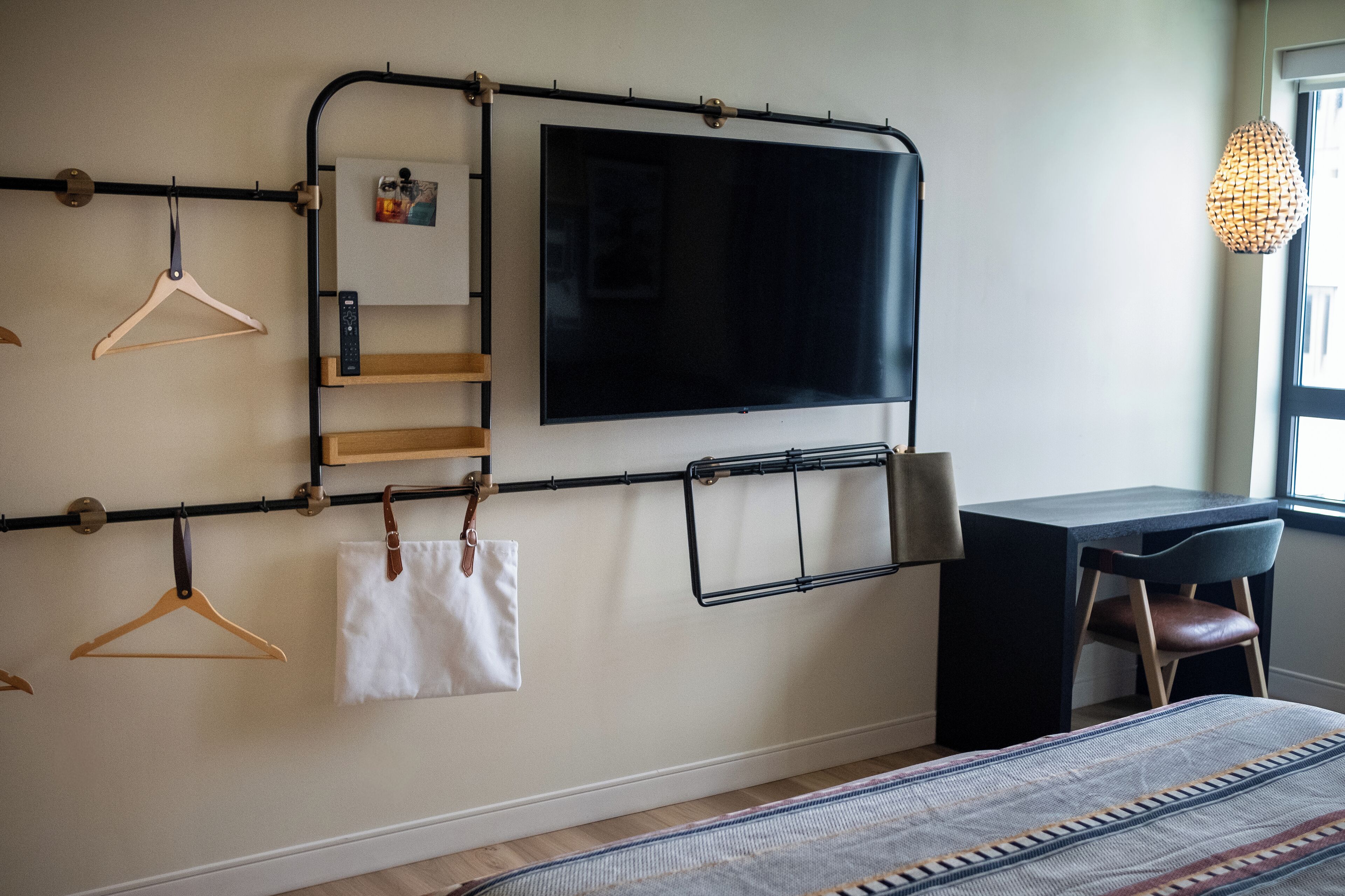 Un dormitorio con cama, escritorio, silla, televisor montado en la pared y ventana.