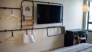 Un dormitorio con cama, escritorio, silla, televisor montado en la pared y ventana.