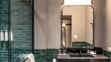A bathroom with a glass shower enclosure, a black sink with a mirror above it, and toiletries on the wall.