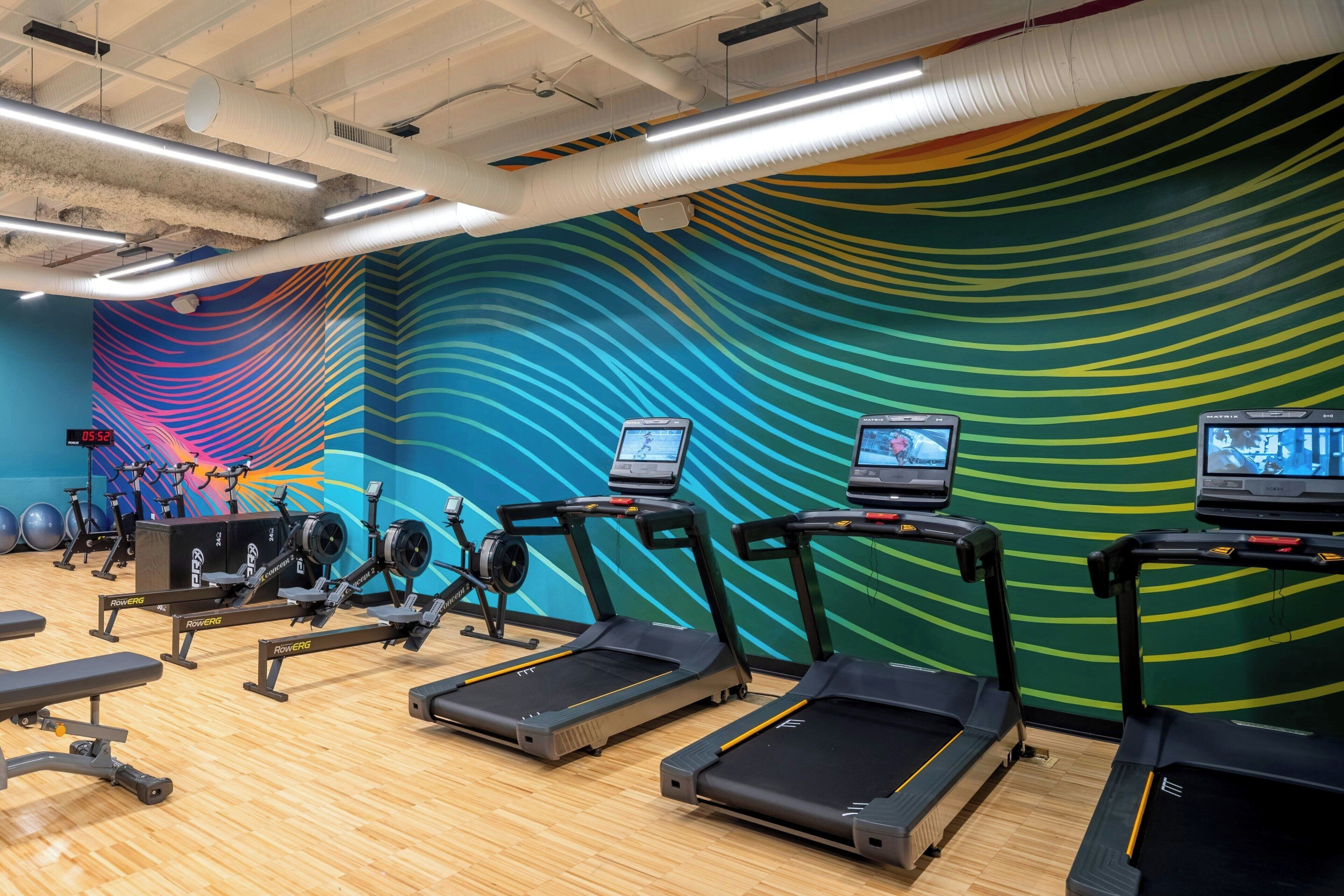 A gym with treadmills, weight machines, and a colorful wall mural.